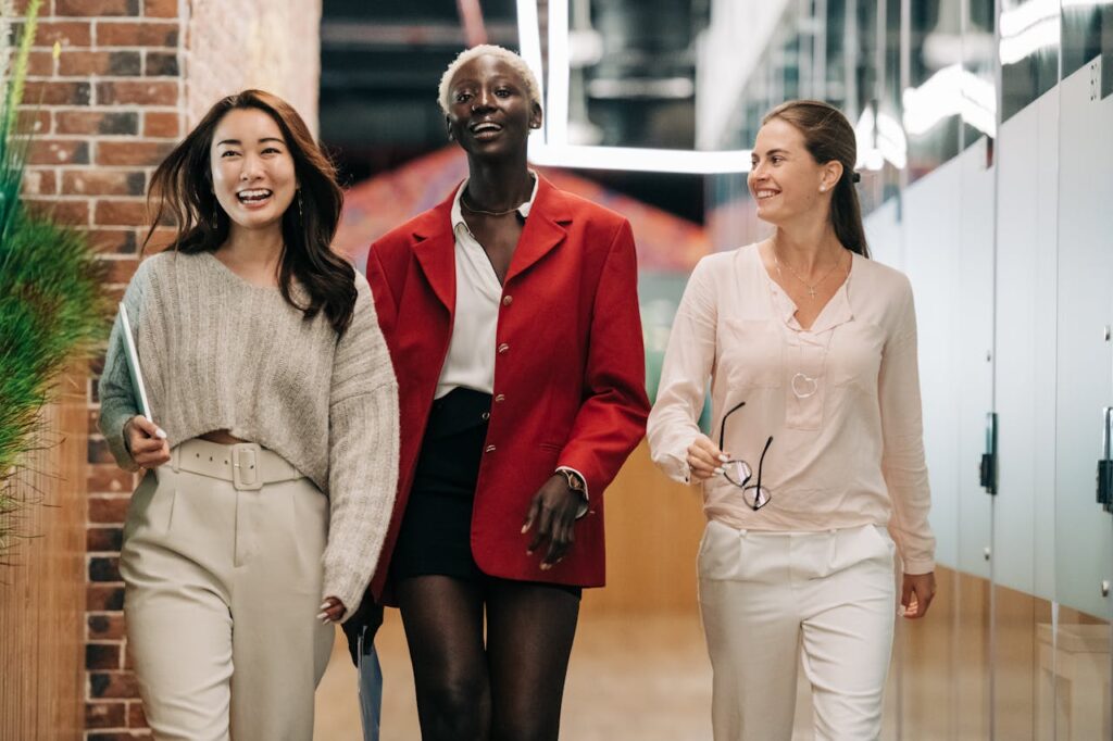Three diverse and confident businesswomen walking together in a modern office hallway, exuding professionalism and joy.
