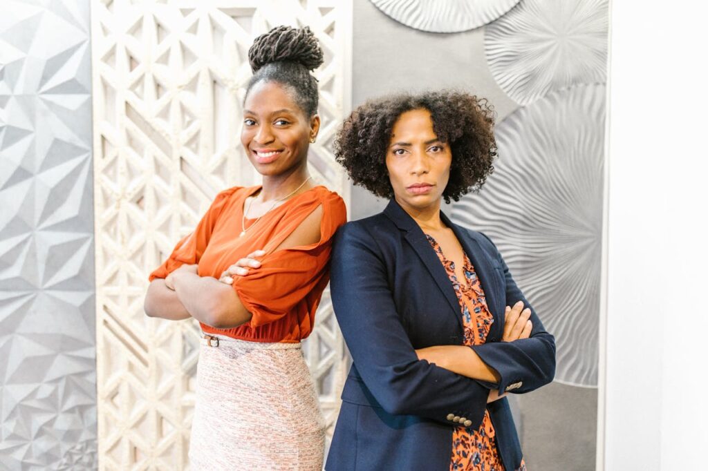 Two professional women with arms crossed in a modern office, exuding confidence and leadership.