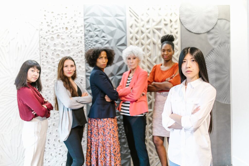 Six diverse women standing confidently with arms crossed in a modern interior setting.
